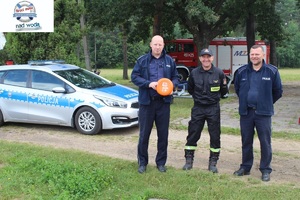 Przed zbiornikiem radiowóz, 2 policjantów. strażak.