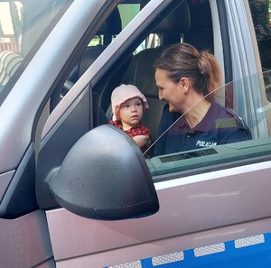Policjantka kuca przy radiowozie, za kierownica siedzi mała dziewczynka.