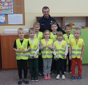 Policjant i dzieci w kamizelkach odblaskowych.