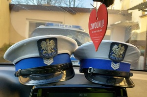 Dwie czapki policjantów ruchu drogowego na pulpicie radiowozu.